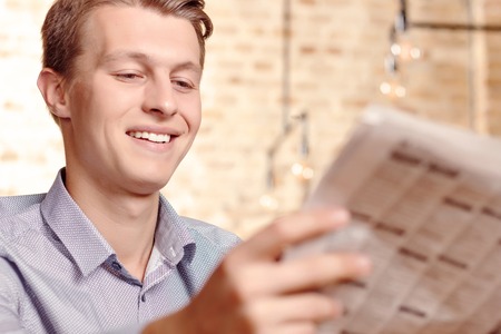 Read with smile. Portrait of young attractive man sitting in cafe and reading newspaper.の写真素材