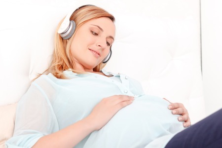Listening together. Portrait of beautiful loving pregnant lady lying on bed and listening to music.の写真素材