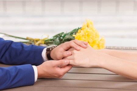 Holding fast. Man holding hands of his lovely girlfriend on background of flowers.の写真素材