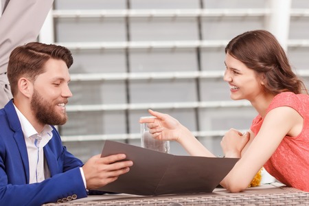 Lets choose it. Portrait of smiling attractive woman and handsome man in cafe holding price list.の写真素材