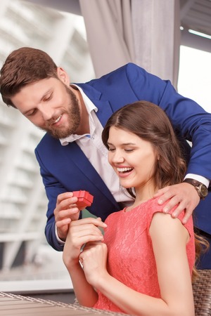 Pleasant surprise. Handsome young man holding ring case and standing behind his girlfriend with closed eyes.の写真素材