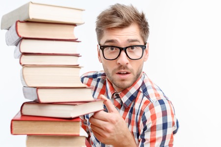 Slave at my book. Surprised serious student holding books and wearing glasses while standing...