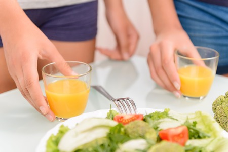 Healthy way of life. Close up of hands of  nice girls holding glasses on the table and standing in...