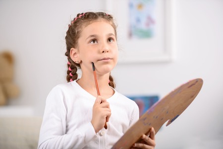 My future picture. Pleasant reflective little holding palette and keeping brush near chick while thinking out her painting.の写真素材