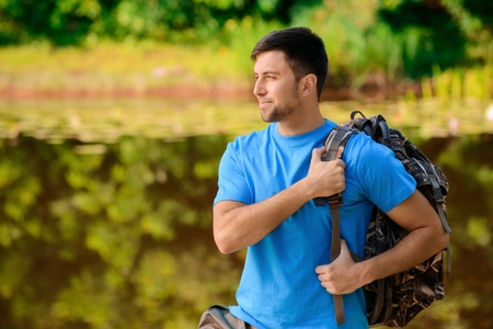 In harmony with nature. Nice blissful handsome man wearing bag and looking aside while reveling in fair weather.の写真素材