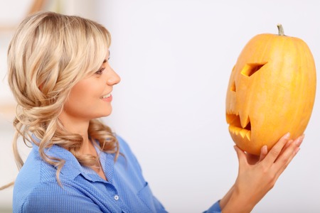 Peace of art. Pretty cheerful happy woman holding pumpkin and looking at it while feeling elatedの写真素材