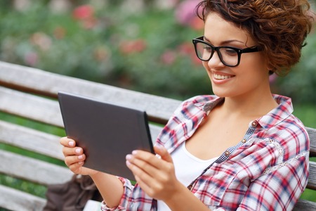 Just having rest. Pleasant young upbeat girl holding laptop and sitting on the bench while evincing...