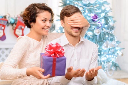 Present for you. Positive cheerful charming girl closing eyes og her boyfriend and going to make surprise for himの写真素材