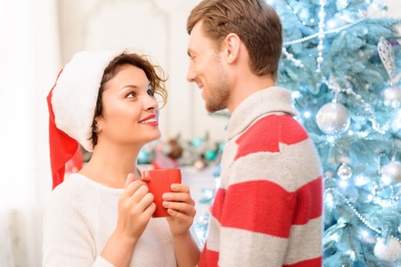 Love you tender. Loving blissful young couple standing near Christmas tree and looking at each other while evincing foundness.の写真素材