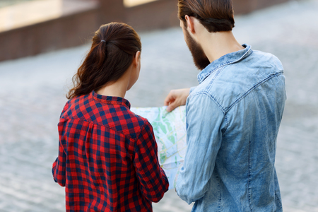Where is the way. Pleasant young tourists holding map and looking for a right route while standing turned backの写真素材
