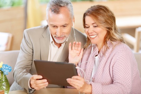 Brisk conversation. Pleasant cheerful happy adult couple holding laptop and having conversation in...