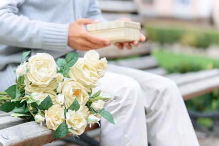 Ready for a date. Close up of bouquet of flowers lying on the bench with man holding present in the...
