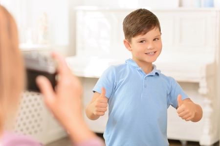 Say cheese. Pleasant cheerful little boy thumbing up and expressing gladness while posing in front of the cameraの写真素材