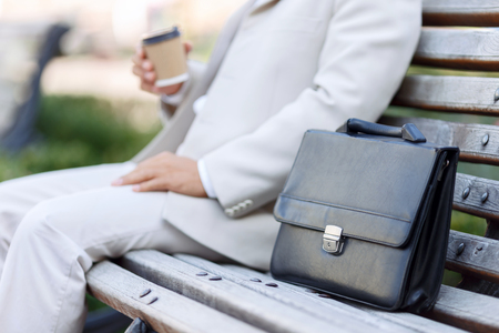 Just relax. Pleasant adult man drinking coffee an having relaxation while sitting on the benchの写真素材
