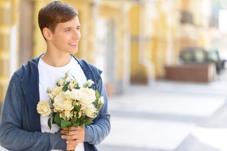 Ready for a date. Pleasant cheerful handsome young guy looking aside and holding bouquet of flowers while feeling happyの写真素材