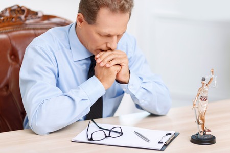 What to do. Serious concentrated professional lawyer holding hands together and thinking out while sitting at the tableの写真素材