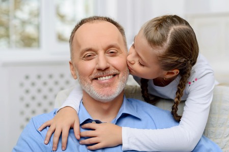 Love you so  much. Upbeat  pretty little girl embracing her grandfather and kissing him while expressing joyの写真素材
