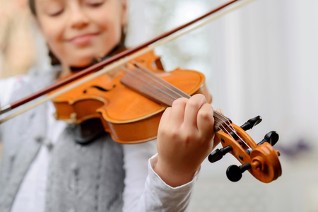 A way to success. Close up of pleasant vivacious pretty girl holding fiddle bow and learning to play the violinの写真素材
