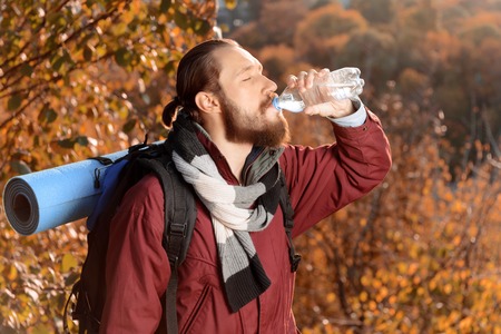 Cheerful positive bearded man holding bottle with water and drinking it while travelingの写真素材