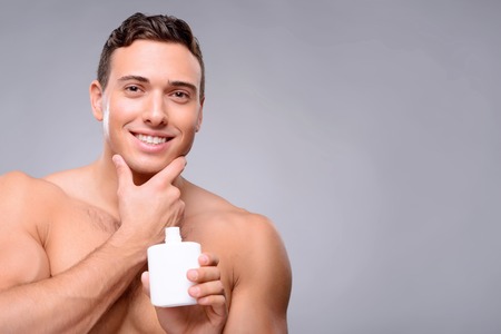 Handsome pleasant man holding lotion and using it while taking care of himselfの写真素材