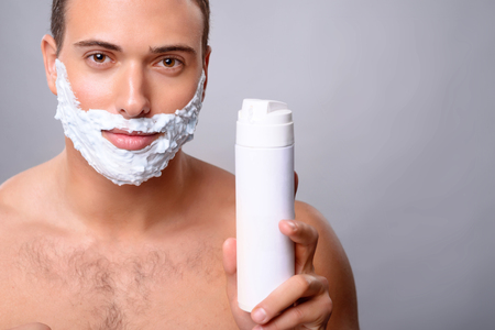 Pleasant handsome upbeat man holding shaving lather and going to shave while feeling confidentの写真素材