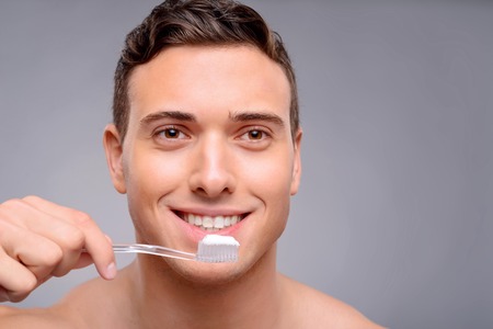 Pleasant smiling handsome guy holding toothbrush and going to clean teeth while evincing joy