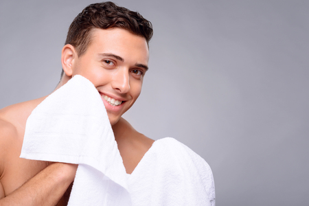 Pleasant vivacious handsome guy holding towel near his face and smiling  after getting a showerの写真素材