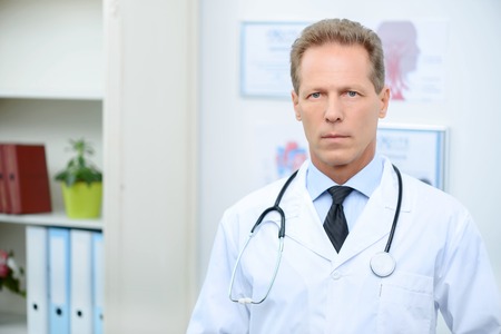 Pleasant serious handsome adult doctor expressing confidence and standing at workの写真素材