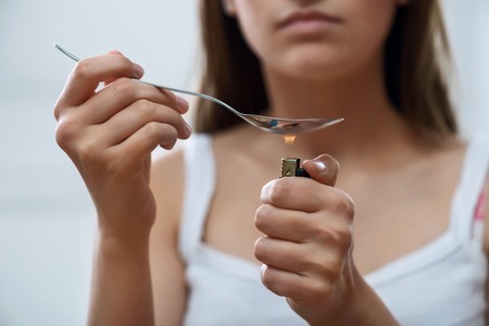 Depressed exhausted young girl holding lighter and spoon while going to take drugsの写真素材