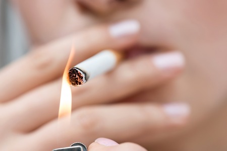 Close up of cigarette in hands of unhealthy girl lighting it and smokingの写真素材