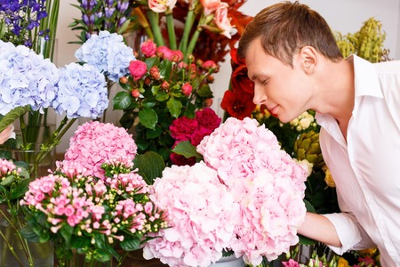 Pleasant handsome upbeat man smelling the flowers and expressing delight while going to buy themの写真素材