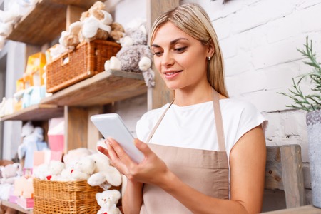 Pleasant charming professional florist holding mobile phone and keeping glance down while restingの写真素材