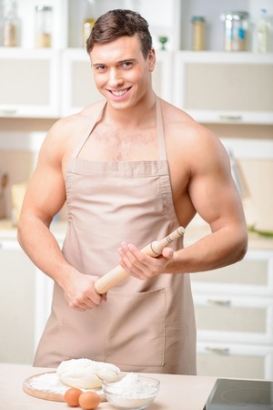 Young attractive male cook holding a battledore is in process of making dough.の写真素材