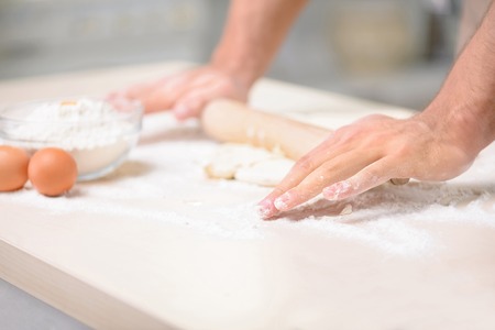 Young athletic male cook occupied with stretching freshly made dough for baking pastry.の写真素材