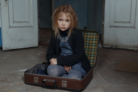 Poor miserable depressed girl holding her hand together and sitting in a suitcase while feeling sadの写真素材