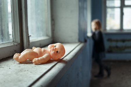 Old little toy lying on the window sill with poor miserable girl standing in the backgroundの写真素材