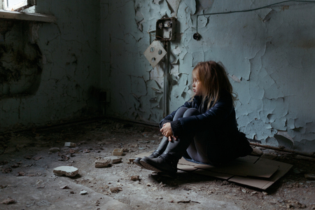 Poor depressed little girl folding her legs and sitting on the floor while looking upの写真素材
