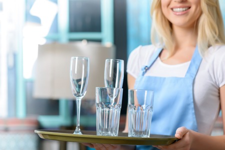 Close up of glasses on the tray in hands of pleasant young waitress while working in the cafeの写真素材