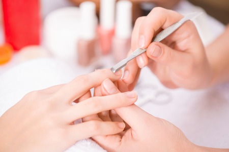 Close up of cuticle pusher in hands of professional manicurist holding it and making manicureの写真素材