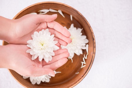 Top view of white beautiful flower in hands of woman holding it on the spa bowl with waterの写真素材