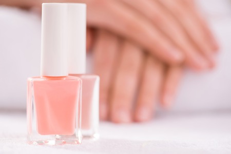 Close up of bottle of nail polish standing on the table with tender hands lying in the backgroundの写真素材