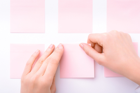 Close up of sticker in hands of professional businesswoman holding it and gluing on the wall while doing her jobの写真素材