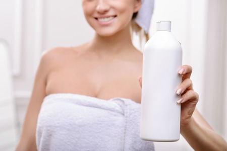 Selective focus of while bottle in hands of positive delighted young woman holding it after taking bath and expressing joyの写真素材