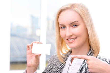 Pleasant content charming adult businesswoman holding little card and pointing it while smilingの写真素材
