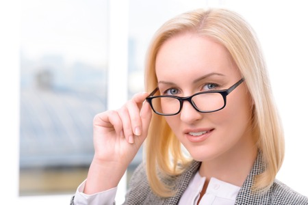 Pleasant positive beautiful businesswoman keeping her glasses and expressing confidence while being involved in workの写真素材