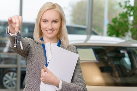 Young female salesperson is offering car keys to a client after closing the deal.の写真素材