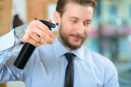 Best professional. Close up of hairspray in hands of professional barber holding it and using it while making hairstyleの写真素材