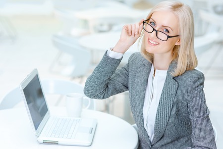 Have a rest. Pleasant smiling attractive business woman holding her glasses and sitting at the table while resting in the cafeの写真素材