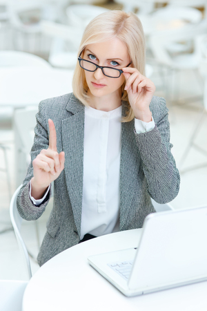Follow the rules. Serious strict business woman holding her finger up and looking at you  while sitting in the cafeの写真素材