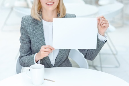 Minimalism in mind. Pleasant overjoyed  woman holding sheet of paper and sitting at the table while evincing joyの写真素材